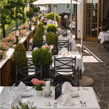 Ein gemütliches Restaurant mit gedeckten Tischen im Freien. Die ansprechend dekorierten Tische sind umgeben von Pflanzen und Sonnenschirmen.