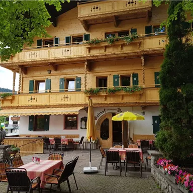 Ein charmantes Holzgebäude mit grünen Fenstern und einem einladenden Außenbereich. Tische und Stühle stehen draußen, umgeben von Bäumen und Blumen.