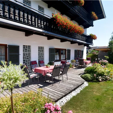 A charming house with a lovely garden seating area and blooming plants. The sunny balcony is decorated with flowers and invites relaxation.