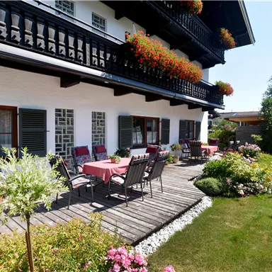 A charming house with a lovely garden seating area and blooming plants. The sunny balcony is decorated with flowers and invites relaxation.