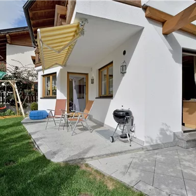 Ein gemütlicher Außenbereich mit Gartenmöbeln. Im Hintergrund ist eine Schaukel und ein Grill zu sehen.