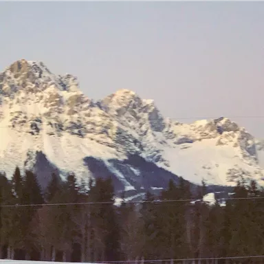 Eine beeindruckende Berglandschaft mit schneebedeckten Gipfeln und einem klaren Himmel. Die Wälder im Vordergrund vervollständigen das malerische Bild.