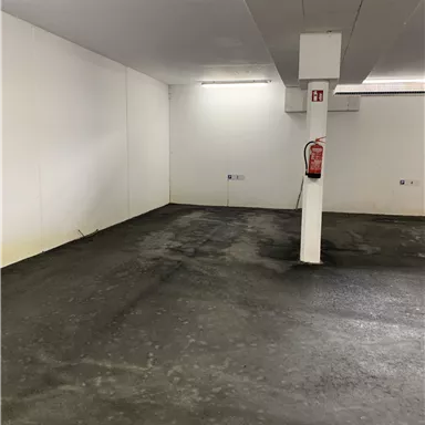 Ein leerer Raum mit Betonboden und weißen Wänden. An der Wand hängt ein Feuerlöscher.