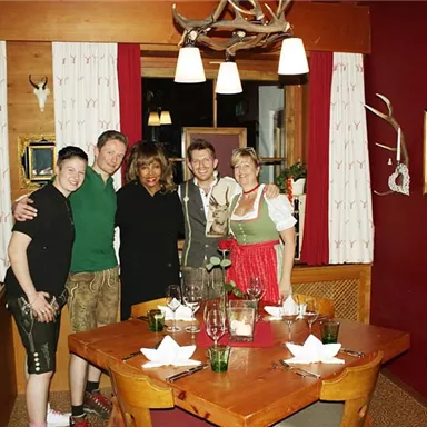 Eine Gruppe von fünf Personen posiert in einem gemütlichen Restaurant. Der Tisch ist liebevoll gedeckt und die Wände sind mit traditionellen Bildern dekoriert.