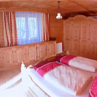 A cozy bedroom with wooden paneling and red accents. There are two beds and a spacious wardrobe.