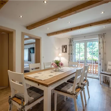 Ein gemütlicher Essbereich mit einem großen Tisch und hellen Stühlen. Das Zimmer hat große Fenster und Holzdecken, die eine einladende Atmosphäre schaffen.