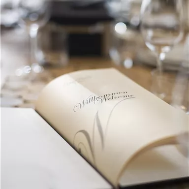 Ein offenes Menü auf einem Tisch mit Gläsern und eleganter Tischdeko. Die Atmosphäre ist gemütlich und einladend.