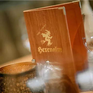 Ein elegantes Restaurant mit einem Menü in Holzoptik. Gläser und eine dekorative Kerze ergänzen das Ambiente.