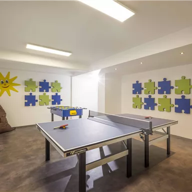 A bright leisure room with a table tennis table and a foosball table. The walls are cheerfully decorated with colorful puzzle shapes.