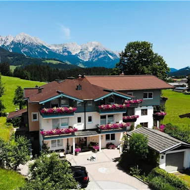 A picturesque house in nature with flower boxes on the balconies. In the background, the majestic mountains and a blue sky are visible.