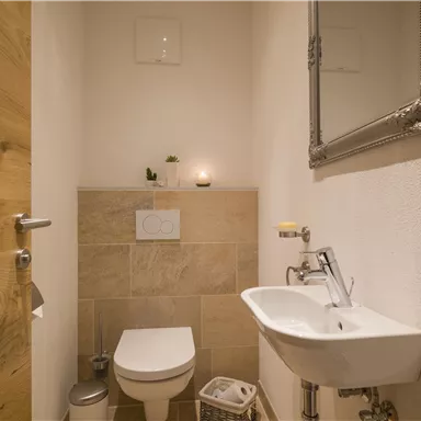 A modern bathroom with a toilet and a small sink. The walls are light, and a large mirror reflects the relaxed atmosphere.