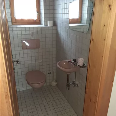 Ein kleines Badezimmer mit hellen Fliesen und einer Dusche. Es gibt ein Waschbecken und eine Toilette in sanften Farbtönen.