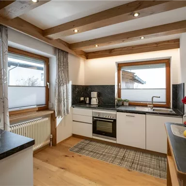 Eine moderne Küche mit Holzdeckenbalken und großen Fenstern. Der Raum ist hell und freundlich, mit einem minimalistischen Design und geräumigen Arbeitsflächen.