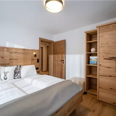 Ein gemütliches Schlafzimmer mit einem großen Doppelbett und Holzdetails. Die Wände sind hell, und im Raum gibt es praktische Möbelstücke aus Holz.