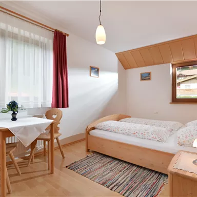 A cozy bedroom with a double bed and a table. Large windows provide plenty of daylight and a pleasant atmosphere.