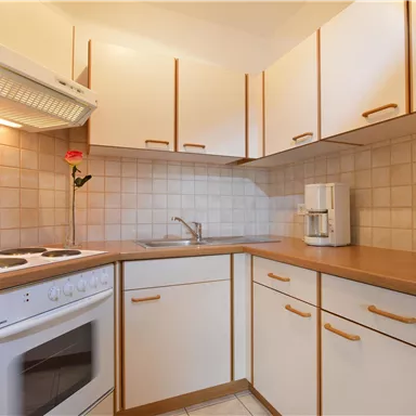 A bright kitchen with modern cabinets and a pleasant atmosphere. On the countertop, there is a flower, and there is a kitchenette with a stove and sink.