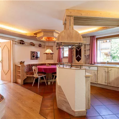 Eine einladende Küche mit Holzregalen und einem runden Tisch. Große Fenster sorgen für viel Tageslicht und eine gemütliche Atmosphäre.