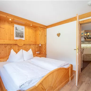 Ein gemütliches Schlafzimmer mit Holzvertäfelung und einem großen Doppelbett. Im Hintergrund ist eine offene Tür zu einer kleinen Küche zu sehen.