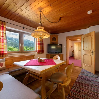 Ein gemütlicher Essbereich mit Holzmöbeln und einem großen Fenster, das einen Blick auf die Berge bietet. Die warmen Farben und das Holzverkleidung sorgen für eine einladende Atmosphäre.