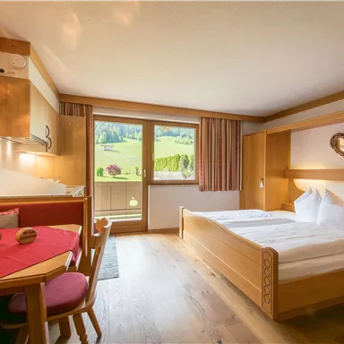 Ein gemütliches Schlafzimmer mit einem Doppelbett und Holz-Möbeln. Der Raum hat große Fenster mit Blick auf die Landschaft und eine kleine Sitzecke.