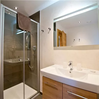 Ein modernes Badezimmer mit einer Dusche aus Glas und einem eleganten Waschbecken. Die Wände sind in neutralen Farben gehalten und es gibt Holzdetails.