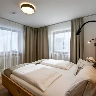 Ein helles Schlafzimmer mit einem großen Bett und weichen Kissen. Die Fenster sind mit einem Vorhang versehen, der viel natürliches Licht hereinlässt.