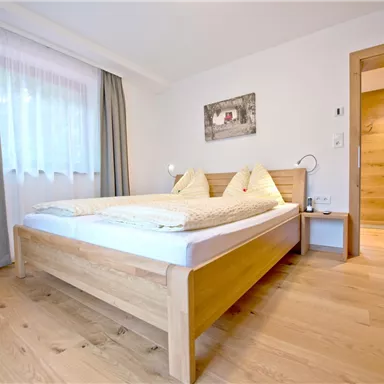 Ein helles Schlafzimmer mit einem gemütlichen Doppelbett und modernen Holzelementen. Die großen Fenster lassen viel natürliches Licht herein.