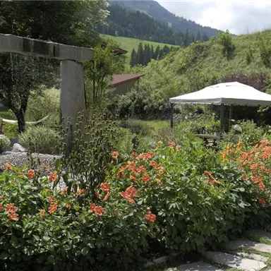A beautiful garden with colorful flowers and stone architecture. In the background, a sun umbrella can be seen, surrounded by green hills.