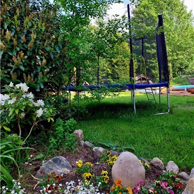 A beautiful garden with colorful flowers and a trampoline. The surroundings are green and inviting.