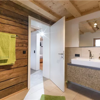 Ein modernes Badezimmer mit einer Holzverkleidung und einem stilvollen Waschbecken. Handtücher in leuchtendem Grün hängen an der Wand.