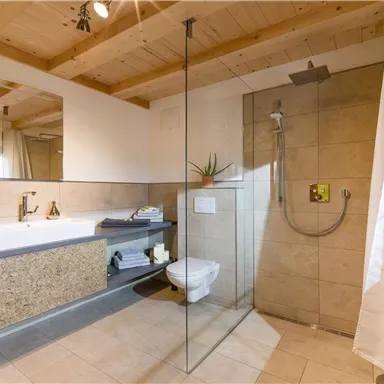 Ein modernes Badezimmer mit einer großen Dusche und einer freistehenden Badewanne. Die Decke ist aus Holz und es gibt helle Fliesen auf dem Boden.