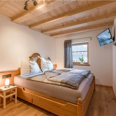Ein gemütliches Schlafzimmer mit Holzmöbeln und einem großen Fenster. Der Raum ist hell und modern eingerichtet, mit einem kleinen Tisch und einem Fernseher an der Wand.