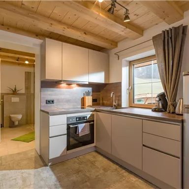 Eine moderne Küche mit Holzregalen und einer hellen Arbeitsfläche. Der Raum ist gut beleuchtet und ganz in neutralen Farben gestaltet.