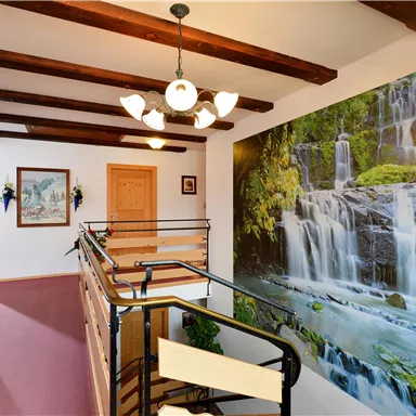 A bright staircase with wooden ceiling beams and a large wallpaper mural of a waterfall. The room is designed to be friendly and inviting.