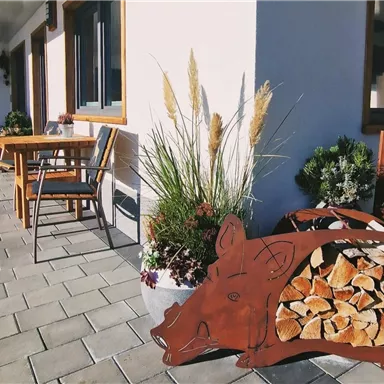 Eine Terrasse mit einem Holzlager in Form eines Schweins und einigen Pflanzen. Es gibt auch einen Tisch und Stühle zum Entspannen.