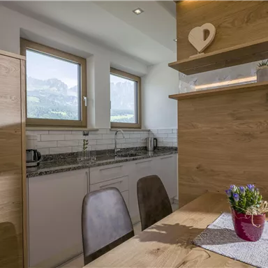 Eine moderne Küche mit Holzdetails und einem Essbereich. Große Fenster bieten einen Blick auf die Berge.