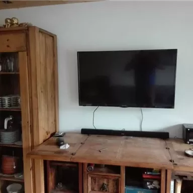 A spacious living room with a TV on the wall. A wooden shelf and a wooden dresser create a cozy atmosphere.