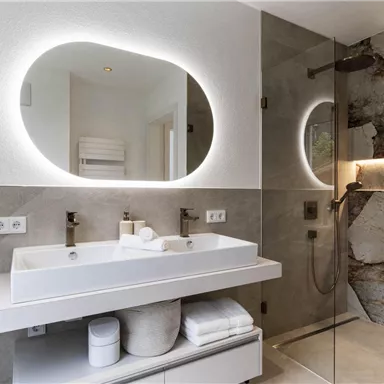 A modern bathroom with an elegant sink and a large mirror. The walls are in soft earth tones, and there is a shower with a glass wall.