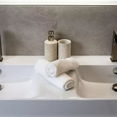 A modern bathroom with two sinks and stylish faucets. Clean, folded towels are placed in the center, creating a relaxing atmosphere.