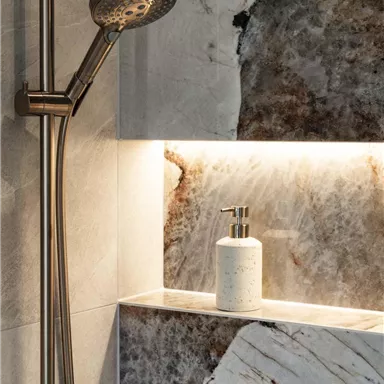 An elegant shower with a modern showerhead and a stylish shelf. The walls are made of beautiful marble with soft lighting.