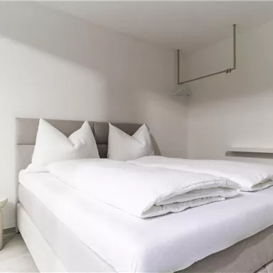 A modern bedroom with a large bed and two pillows. The walls are light and the room feels bright and inviting.