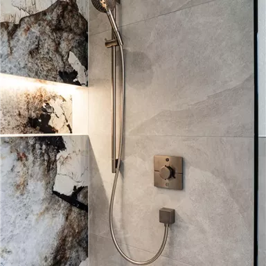 A modern shower with an elegant hand shower. The walls are designed with gray and marbled tiles.