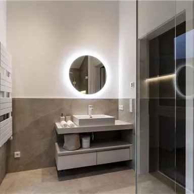 A modern bathroom with a simple sink and a matching round mirror. The walls are in neutral tones, and the light is bright and inviting.