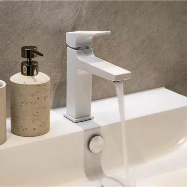 A modern sink with an elegant faucet. Next to the sink are two decorative containers.