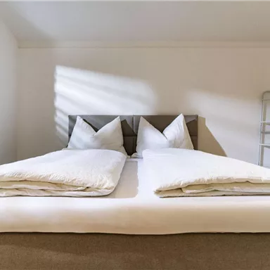 A modern bedroom with a comfortable double bed and fresh white bed linens. Soft light falls through the windows, creating a cozy atmosphere.