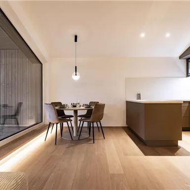 A modern kitchen with a dining table and chairs. Large windows provide plenty of daylight and a bright atmosphere.