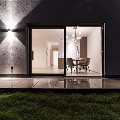 A modern living room with large windows that lead to a terrace with a view of grass. The lighting creates an inviting atmosphere in the evening mood.