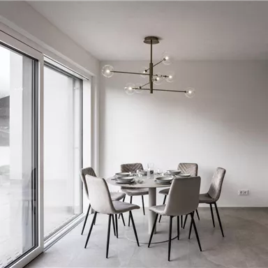 A modern dining room with a round table and elegant chairs. Large windows let in a lot of light and offer a view outside.