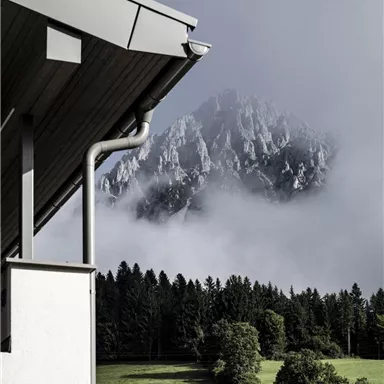 A view of the mountains with fog and green meadows in the foreground. The architecture of the roof harmoniously blends into the landscape.
