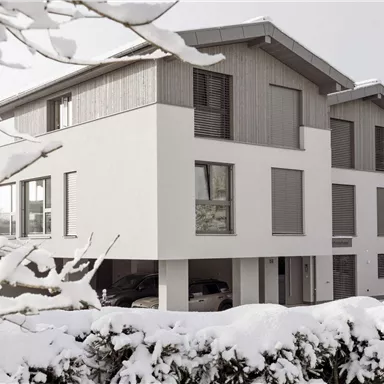 A modern house in winter, surrounded by snow. The architecture combines wood and white, creating a cozy and stylish atmosphere.